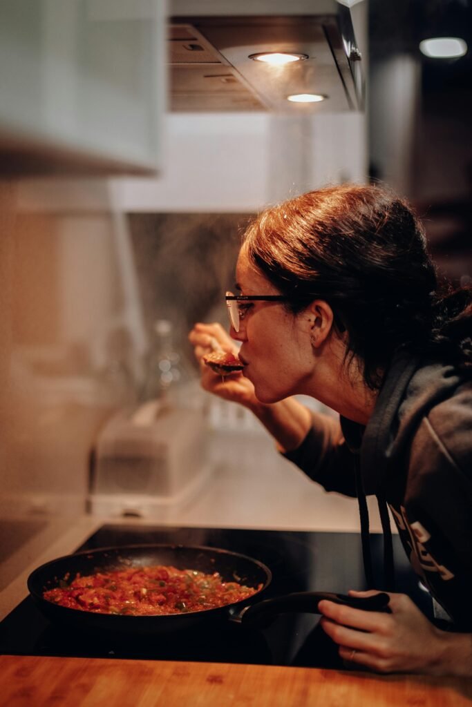 pexels-photo-1587830-1587830 Woman cooking and tasting a dish on the stove, showcasing home culinary expertise.