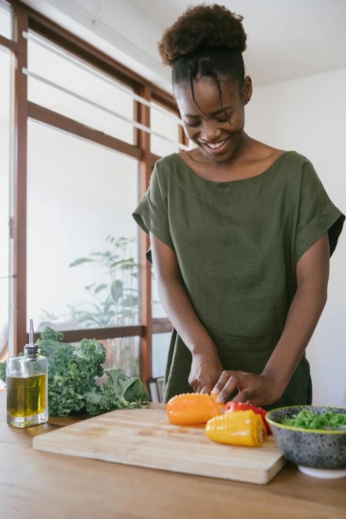 pexels-photo-3622643-3622643 Smiling woman in kitchen slicing bell peppers, promoting healthy eating and joy in food preparation.
